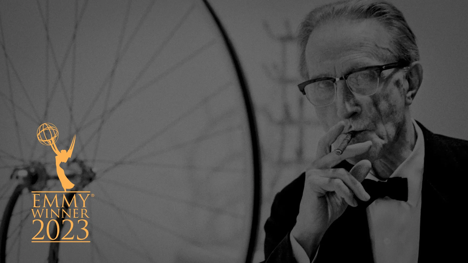 Black-and-white image of Marcel Duchamp in a tuxedo, smoking a cigar beside his sculpture Bicycle Wheel. An Emmy Winner 2023 badge appears on the left.
